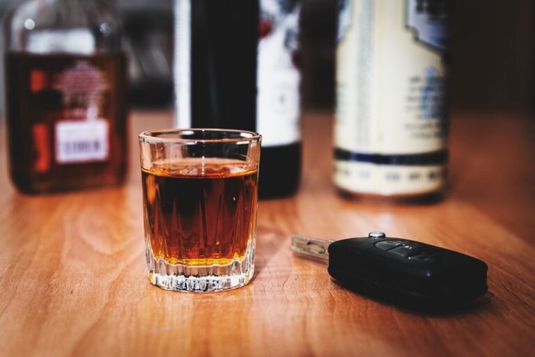 Image is of a car key sitting on a table next to a glass of alcohol and bottles of alcohol in the background, concept of DUI laws in Florida