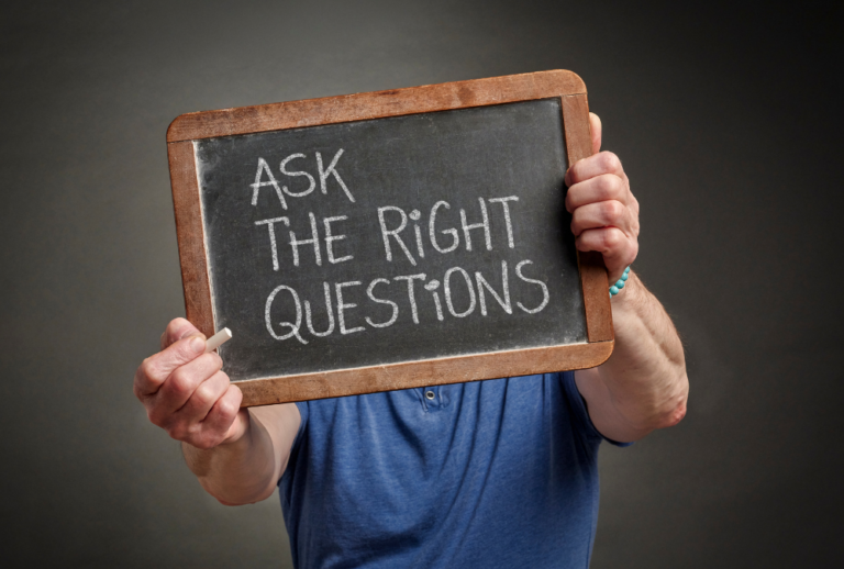 Image is of a man holding up a small slate chalkboard with the words 'ask the right questions' written in white chalk, concept of questions to ask a criminal defense lawyer in Ponte Vedra Beach