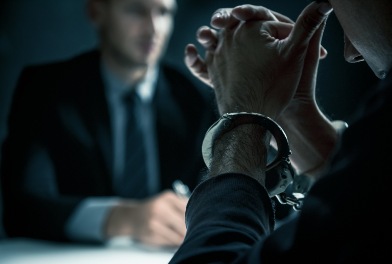Image is of an upset man in handcuffs sitting at a table speaking with an investigator, concept of the insanity defense in Florida