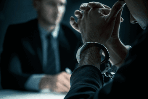 Image is of a handcuffed man sitting at an interrogation table with a police detective, concept of criminal defense lawyer in Palm Valley
