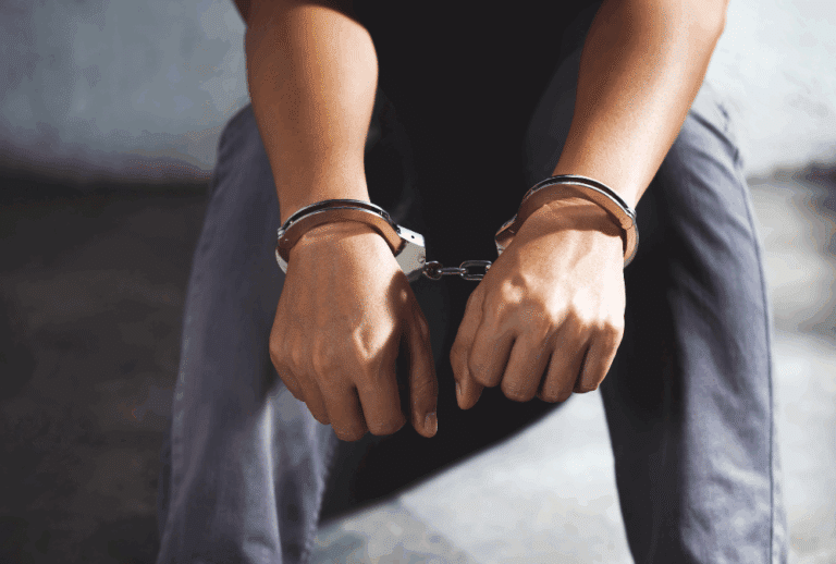 Image is of a teen boy sitting on the ground in a jail cell with his hands cuffed, concept of felony charges on a minor in Jacksonville