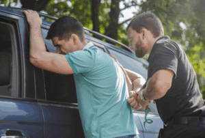 Image is of a man being pushed up against a car by a police officer while being handcuffed, concept of constructive possession in Ponte Vedra Beach