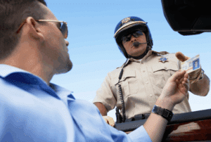 Image is of a man handing his driver's license to an angry highway patrolman after being pulled over, concept of how an out-of-state DUI can affect your Florida license
