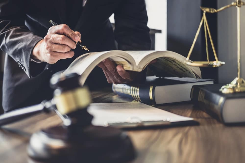 Lawyer reading law book beside gavel and scales in courtroom