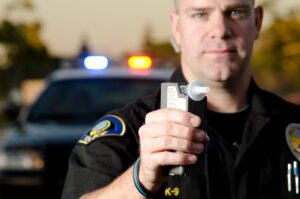 Image is of a police officer holding a breathalyzer device toward a driver, concept of roadside testing procedures at DUI checkpoints in Ponte Vedra Beach.