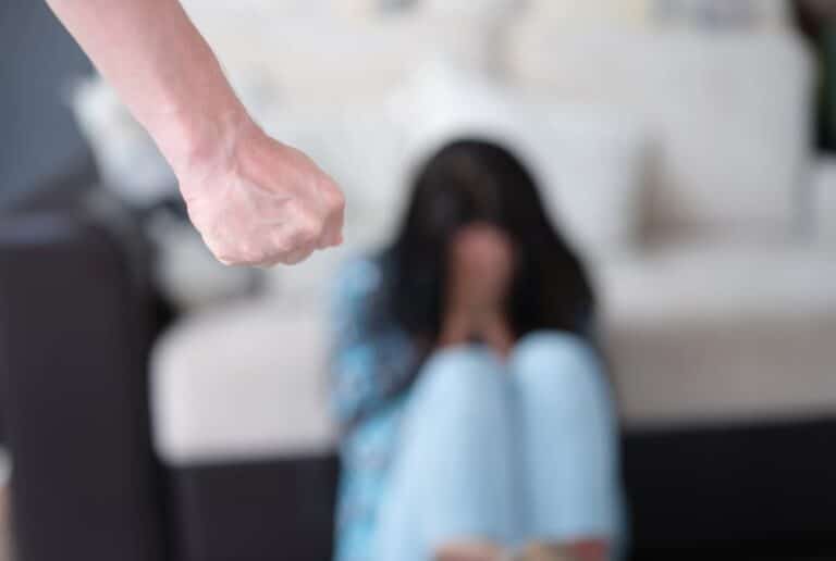 Image shows a frightened woman sitting on the floor with a raised fist nearby illustrating Underage domestic violence arrests in Ponte Vedra Beach