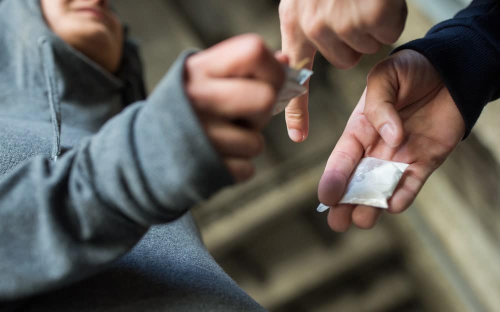 Image is of a person handing over a small packet to another, concept of street-level drug sale and criminal charges
