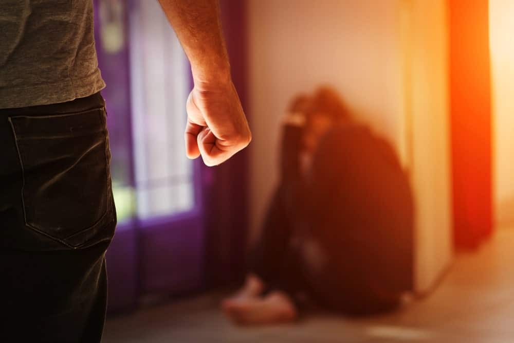 Image is of a tense domestic situation with a distressed individual and an aggressive presence, illustrating the real life context behind domestic violence charges