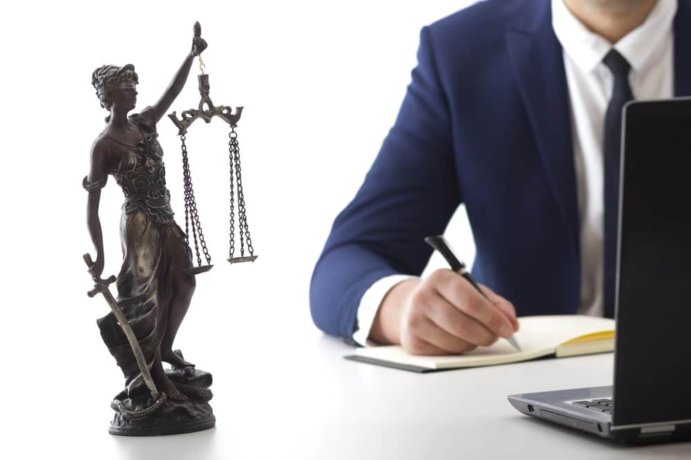 Image is of a Lady Justice statue beside a lawyer reviewing documents at a desk, showing legal analysis related to domestic violence charges and case strategy