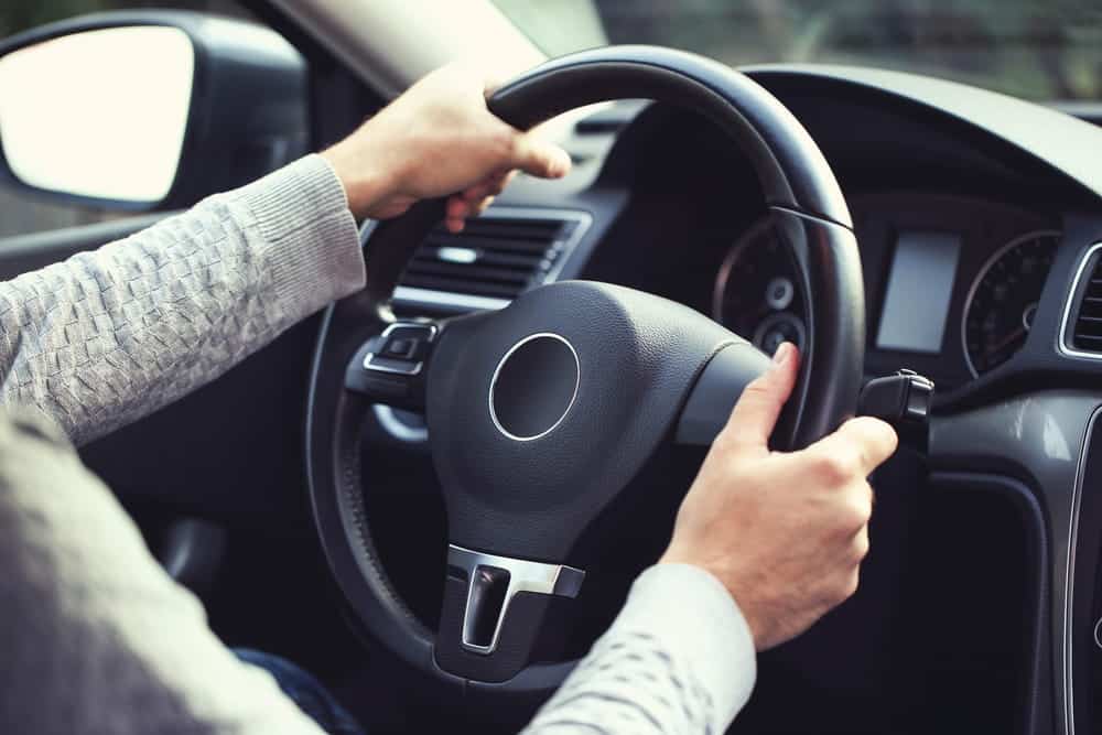 Image is of a driver holding a steering wheel inside a vehicle, concept of DUI charges and how driving decisions affect professional licenses.