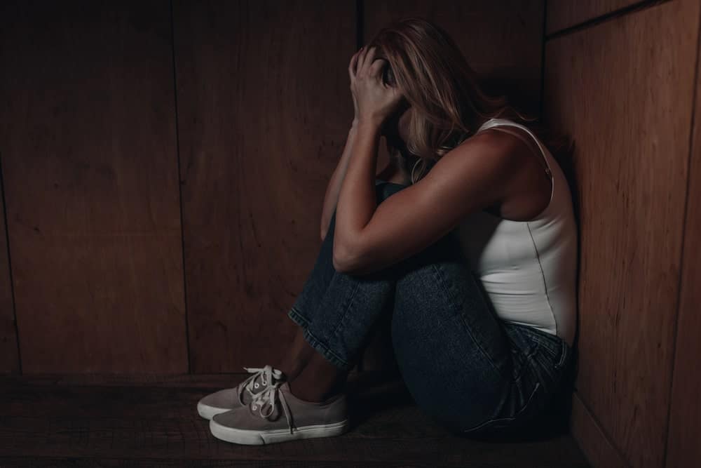 Image is of a woman sitting on the floor holding her head in distress, representing the emotional consequences tied to a DV conviction in Florida