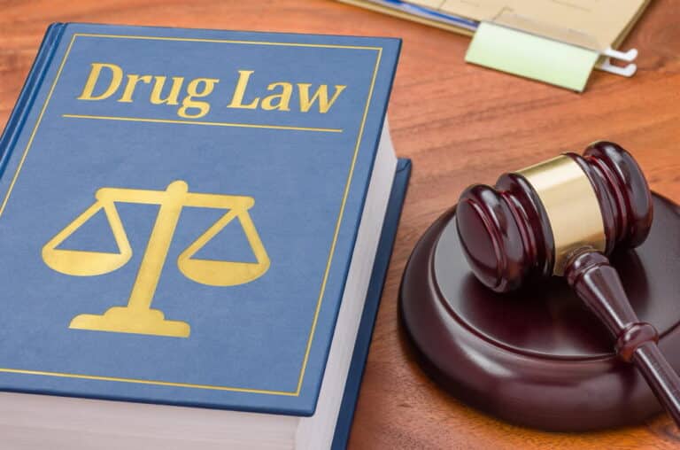 Image is of a legal gavel and drug law textbook on a desk, symbolizing drug charges and legal proceedings