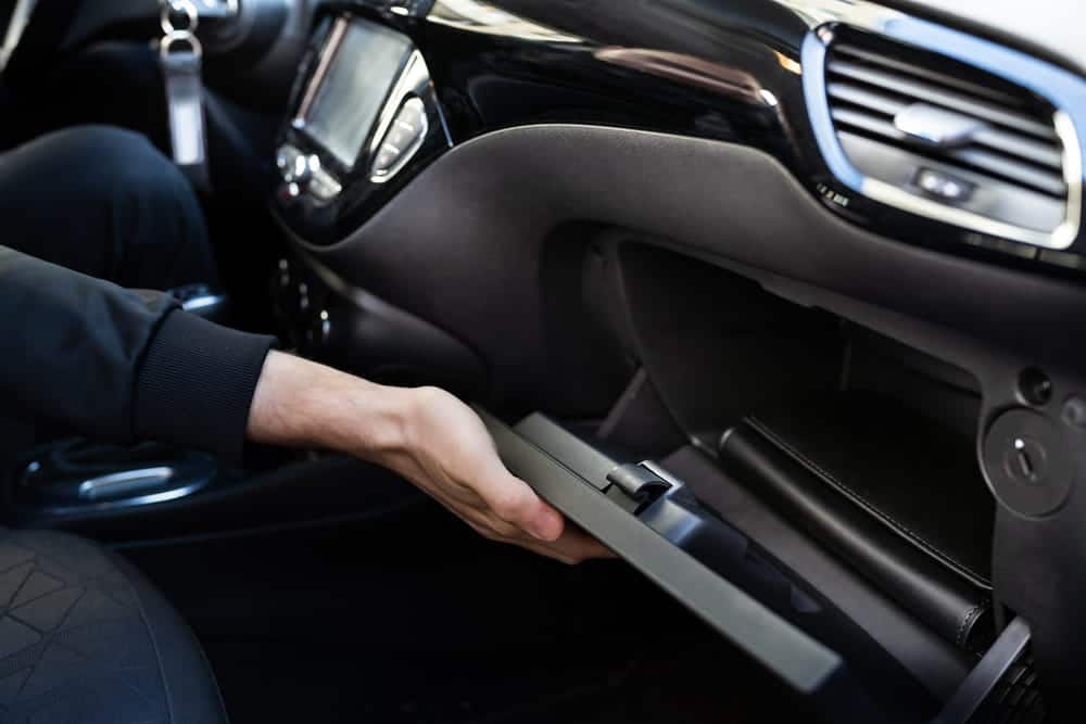 Image is of a person opening a car glove compartment during a search, concept of drug possession in Ponte Vedra investigation and discovery of controlled substances