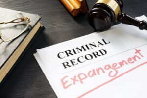 Image is of criminal record expungement paperwork beside a judge’s gavel, concept of removing a past drug charge from public records.