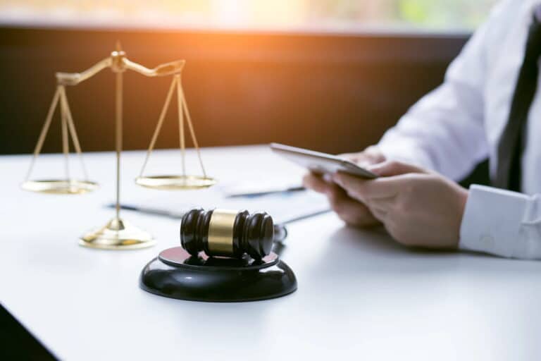 Image is of a person reviewing messages on a phone beside a courtroom gavel and scales of justice, concept of text message evidence used in DV cases.