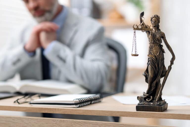 Image is of a Lady Justice statue in a law office with an attorney reviewing case documents, concept of legal defense strategies for a DUI charge.