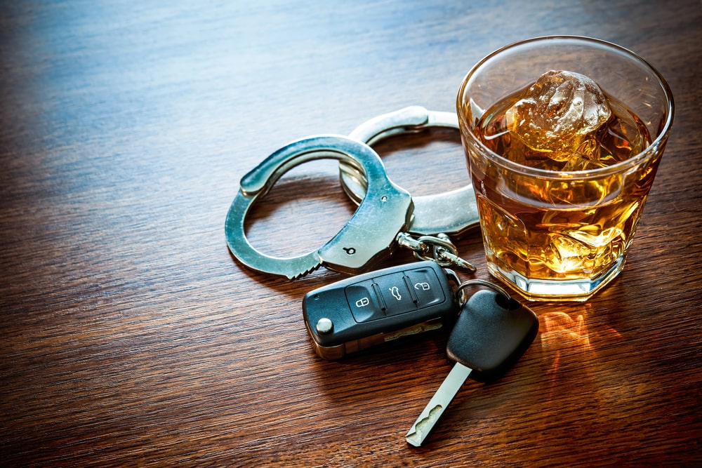 Image is of a glass of alcohol beside car keys and handcuffs, concept of prior DUIs increasing the legal consequences of repeat impaired driving offenses.
