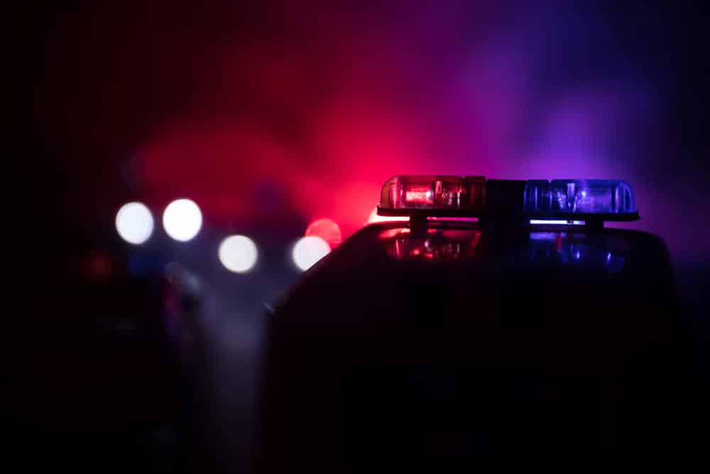Image is of a police vehicle with emergency lights illuminated during a nighttime traffic stop, concept of prior DUIs leading to enhanced criminal investigations and penalties.