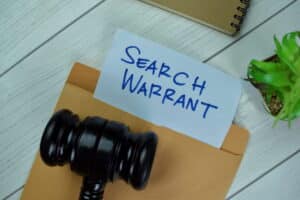 Image is of a search warrant document beside a judge's gavel, concept of search warrants in criminal cases.