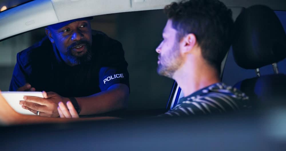 Image is of a police officer speaking with a driver during a traffic stop, concept of search warrants in drug investigations.