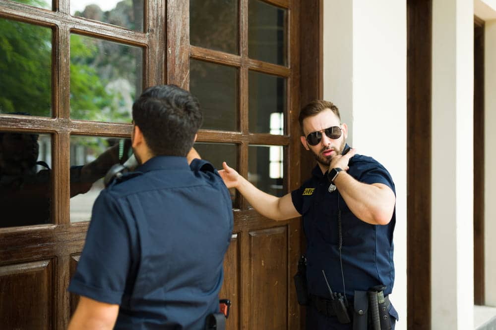 Image is of police officers outside a residence, concept of executing search warrants during drug investigations.