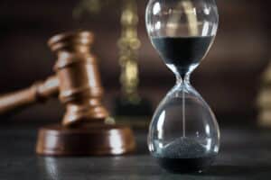 Image is of an hourglass in front of a judge’s gavel, concept of how long a drug case may take in court.