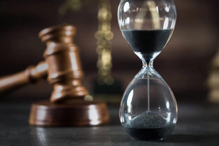 Image is of an hourglass in front of a judge’s gavel, concept of how long a drug case may take in court.