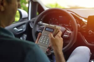 Image is of a driver using an in vehicle breath device, representing ignition interlock rules after a DUI.