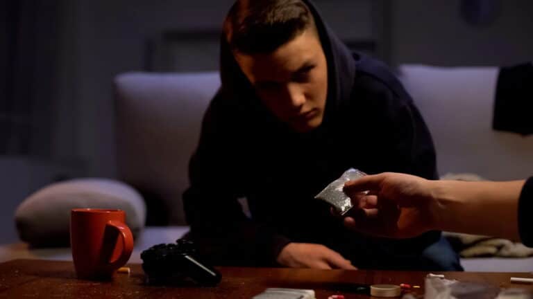 Image is of a young person being shown a small bag of suspected drugs, concept of juvenile drug charges and possession allegations.